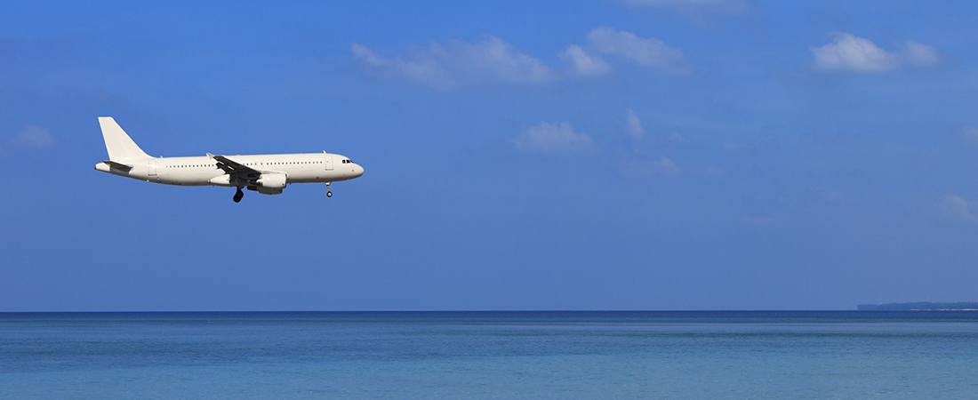 Avión comercial volando a baja altura sobre las aguas cristalinas de un mar azul bajo un cielo despejado.